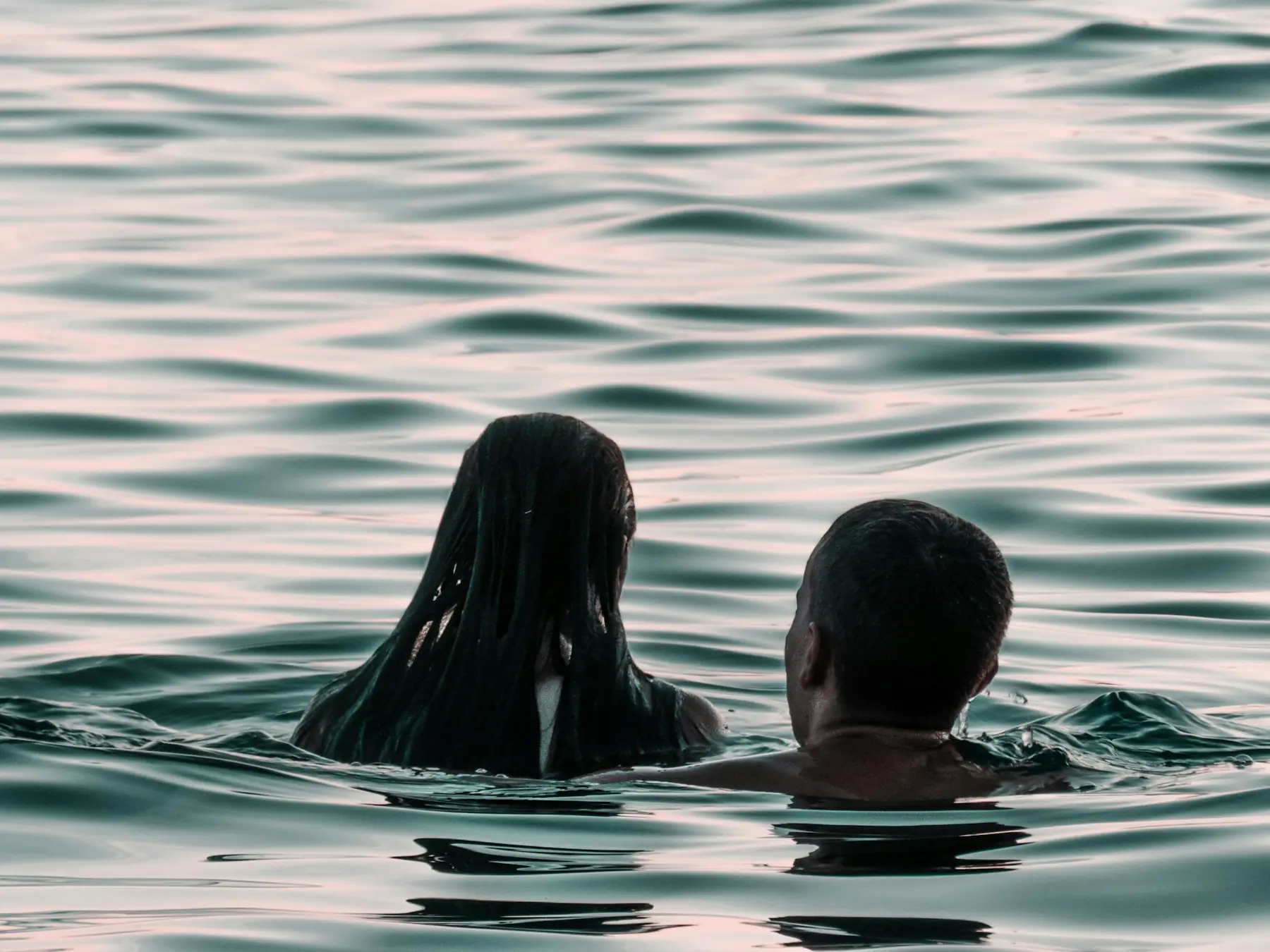 Two people swimming in the sea at dusk